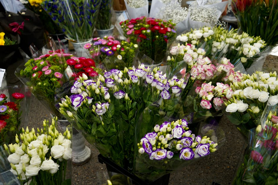 A colorful display of fresh flower bouquets arranged on a worktable, consisting of various flower types including white, pink, purple, and red blooms. The arrangements feature roses, lisianthus, and m