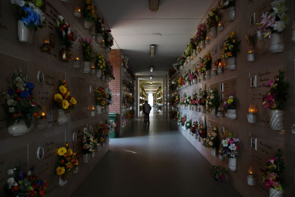 A corridor lined with memorial plaques and white ceramic vases filled with vibrant, fresh floral arrangements, including yellow, pink, purple, and white flowers such as daisies, roses, and tulips. The