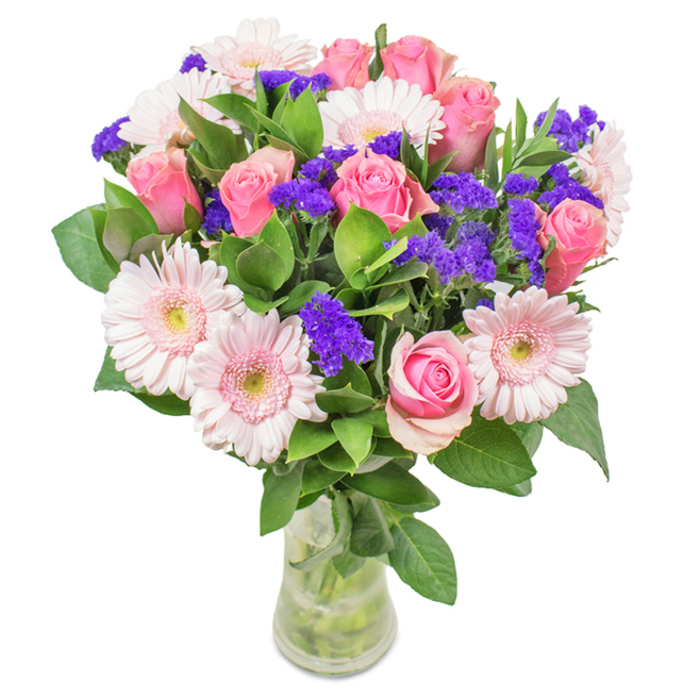 Vibrant and inviting, this floral bouquet-crafted by skilled hands in the heart of Archway-features an exquisite balance of colour and form. Positioned against a pure white backdrop and nestled in a clear glass vase, the display features approximately eight blushing pink roses, some tightly closed, others gently opening in their classic spiral, embodying a sense of unfolding celebration. Intertwined among these are dainty pale pink Gerbera daisies, their wide, ruffled petals radiating out from creamy centers and echoing the cheerful atmosphere found at Archway's local markets. Bright clusters of vivid purple statice lend dramatic contrast, their wild texture reminiscent of carefree walks near Elthorne Park. Anchoring the piece is a lush base of deep green foliage, infusing the bouquet with a sense of abundance and an underlying note of woodland freshness. The transparency of the vase highlights the careful arrangement of stems and fresh water, reinforcing the freshness of a same-day Archway flower delivery. This thoughtfully composed bouquet is an ideal choice for birthdays, anniversaries, or as a welcoming accent for homes and businesses across Archway, Holloway, and Tufnell Park, sending a heartfelt message of joy, gratitude, or affection.