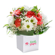 An uplifting, artfully gathered bouquet unfolds its charm from within a pristine white gift bag, its beauty capturing the spirit of Archway's bustling lanes and peaceful green spaces. The central drama is provided by a medley of lush coral and vivid red carnations, their ruffled, cloud-like petals suggesting movement and a gentle, velvety touch. These blooms mingle with pure white daisies whose golden-green centers gleam like little sunbeams, evoking the joy of spring mornings spent in Whittington Park. Stems of baby's breath-tiny, airy, and laced like morning mist-float delicately between the larger flowers, softening the transitions and adding a note of innocence. Notably, a few unopened buds tinged with purple keep secrets of blossoms yet to unfold, bringing intrigue and layered interest. All of this bounty is held within a cocoon of broad, polished deep green leaves that lend stability and contrast, amplifying the fresh vitality of each bloom. The arrangement's full, rounded form and expertly crafted presentation make it an ideal, ready-to-present gift for commemorating birthdays or brightening a loved one's day in Archway. Every stem, chosen and placed with care, speaks to the local florists' understanding of celebration, sentiment, and the comforting presence of fresh flowers delivered with pride and reliability in the North London community.